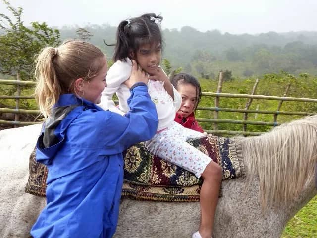 Freiwillige stützt Kind auf Pferd
